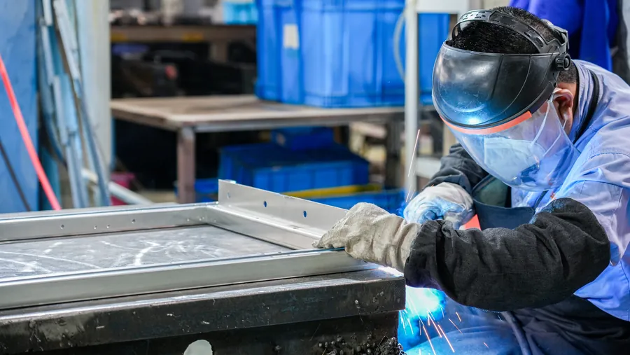 Operator welding a metal cabinet panel at a workbench